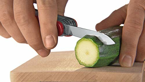 Hands cutting zucchini with a pocket knife on a wooden board.